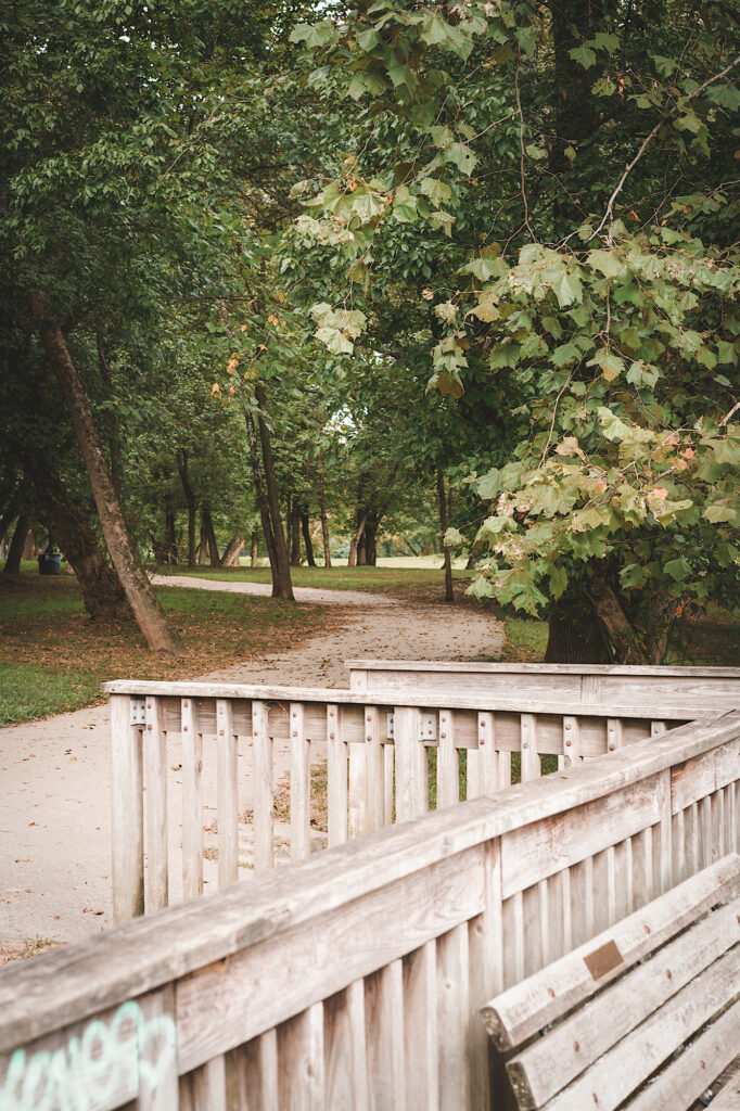 Wooden viewing deck with bench with paved walking path and trees in background