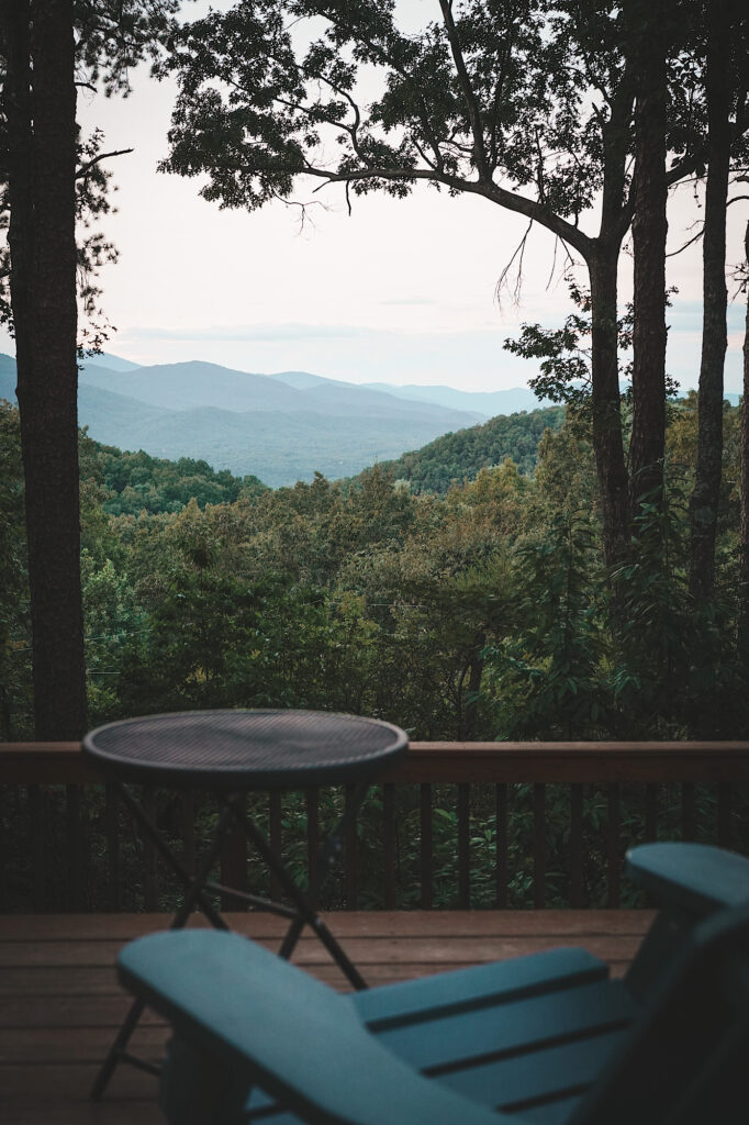 View of mountains from a wooden deck with a chair and small side table