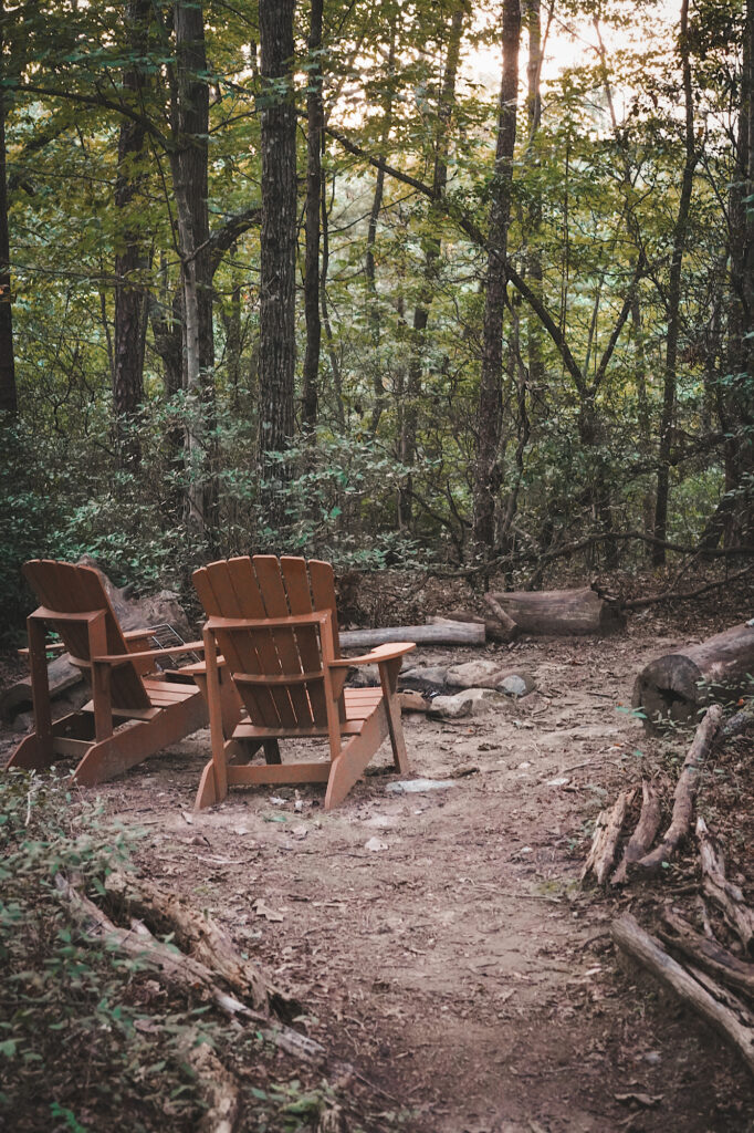 Clearing in woods with 2 wooden chairs and fire pit